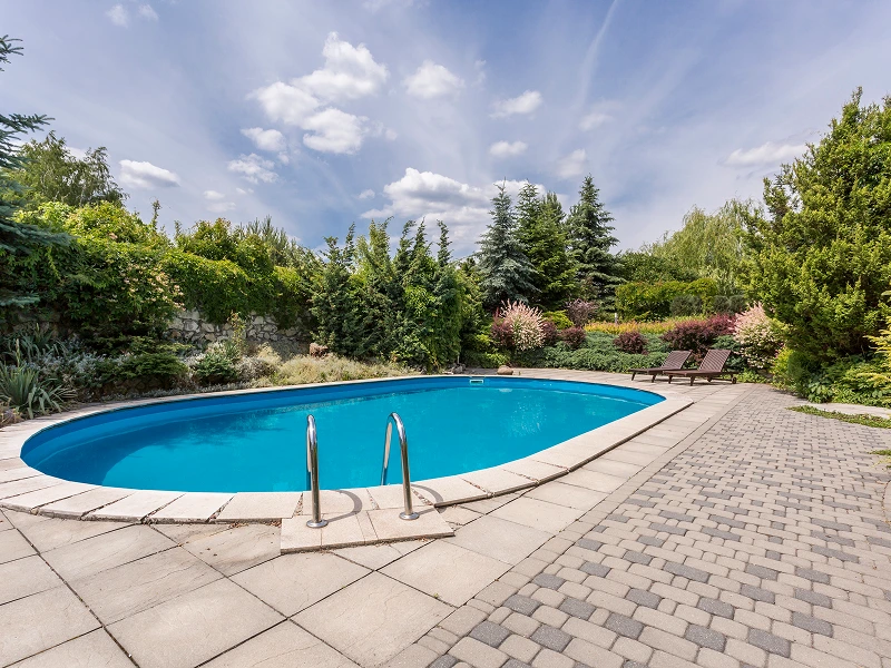 Oval pool, patio, landscaping, sunny day.